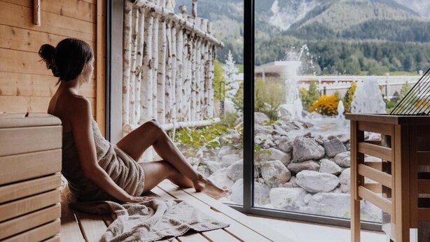 Una persona sentada junto a una ventana con vistas a montañas y un interior de madera.