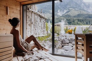 A person sitting by a window with a view of mountains and a wooden interior. - Hotel Riederalm (Leogang)