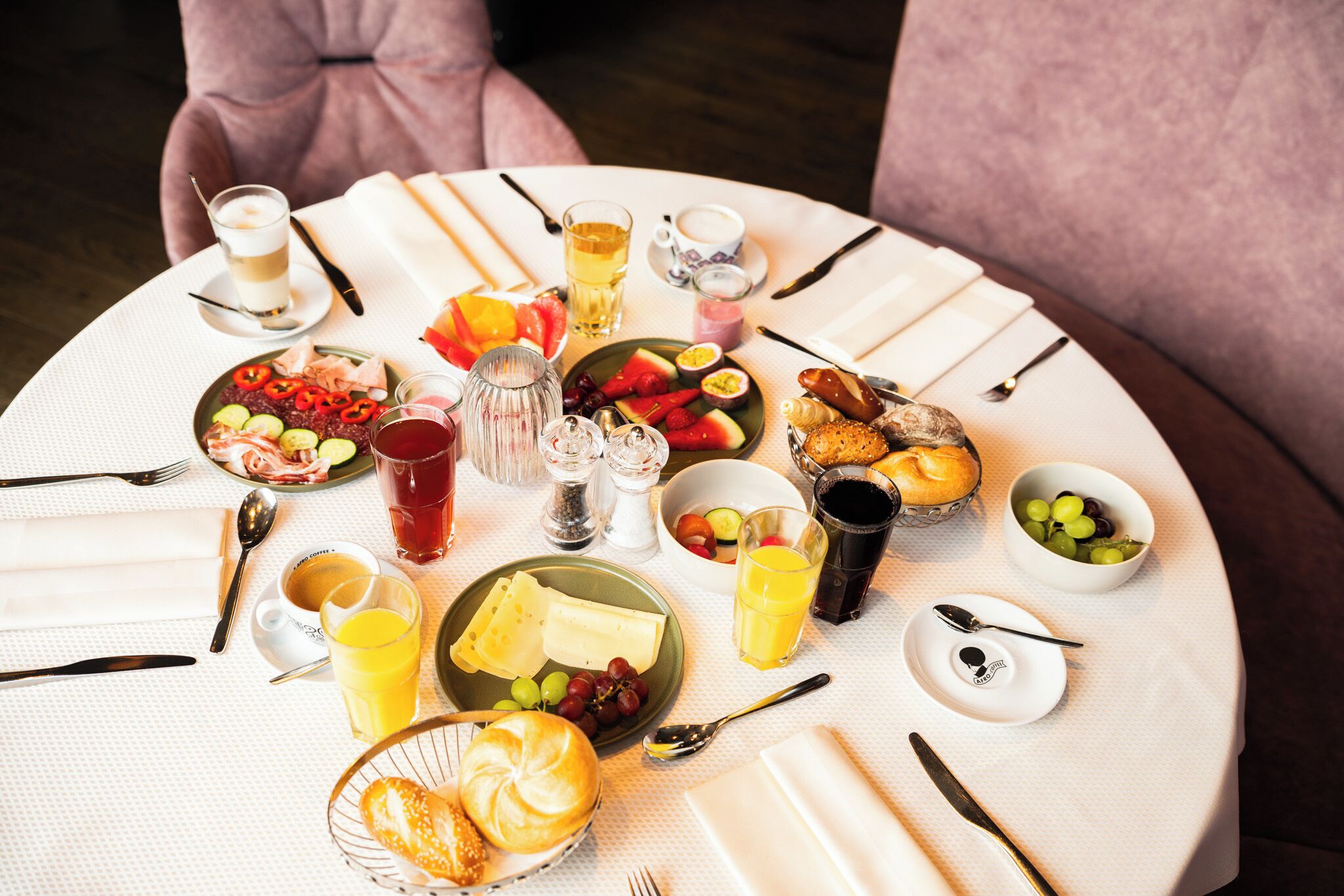 Une table de salle à manger ronde, sur laquelle sont disposés divers aliments pour le petit-déjeuner, notamment des fruits, des viennoiseries et des boissons.