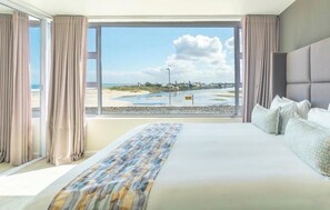 A bedroom with a large bed, a view of the beach, and curtains. - Luxurious Two-bedroom Sea Facing Apartment in Kaapstad (Cape Town)