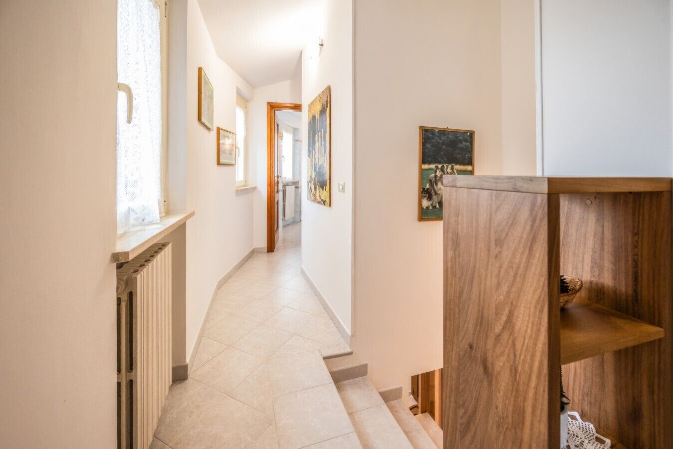 Un couloir avec un radiateur, une étagère en bois et des œuvres d’art encadrées accrochées aux murs.