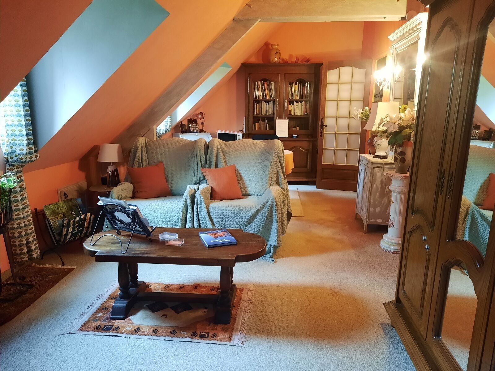 Een gezellige kamer onder de dakrand, met een bank, een bijzettafeltje en een boekenkast.