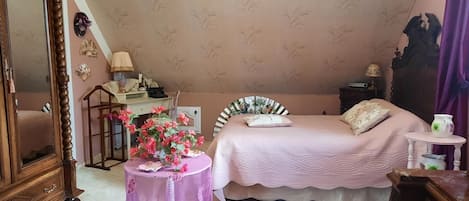 A bedroom with a bed, a dresser, a desk, a chair, and a table with flowers.