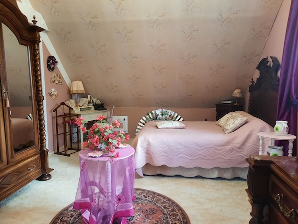 A bedroom with a bed, a dresser, a desk, a chair, and a table with flowers.