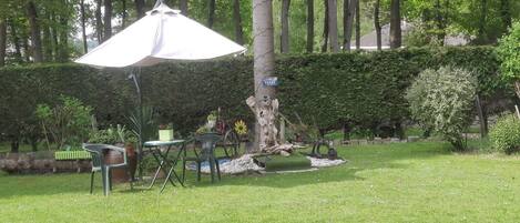 An outdoor seating area with a table and chairs, a tree, and a hedge.