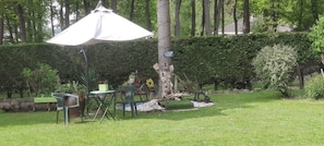 An outdoor seating area with a table and chairs, a tree, and a hedge.