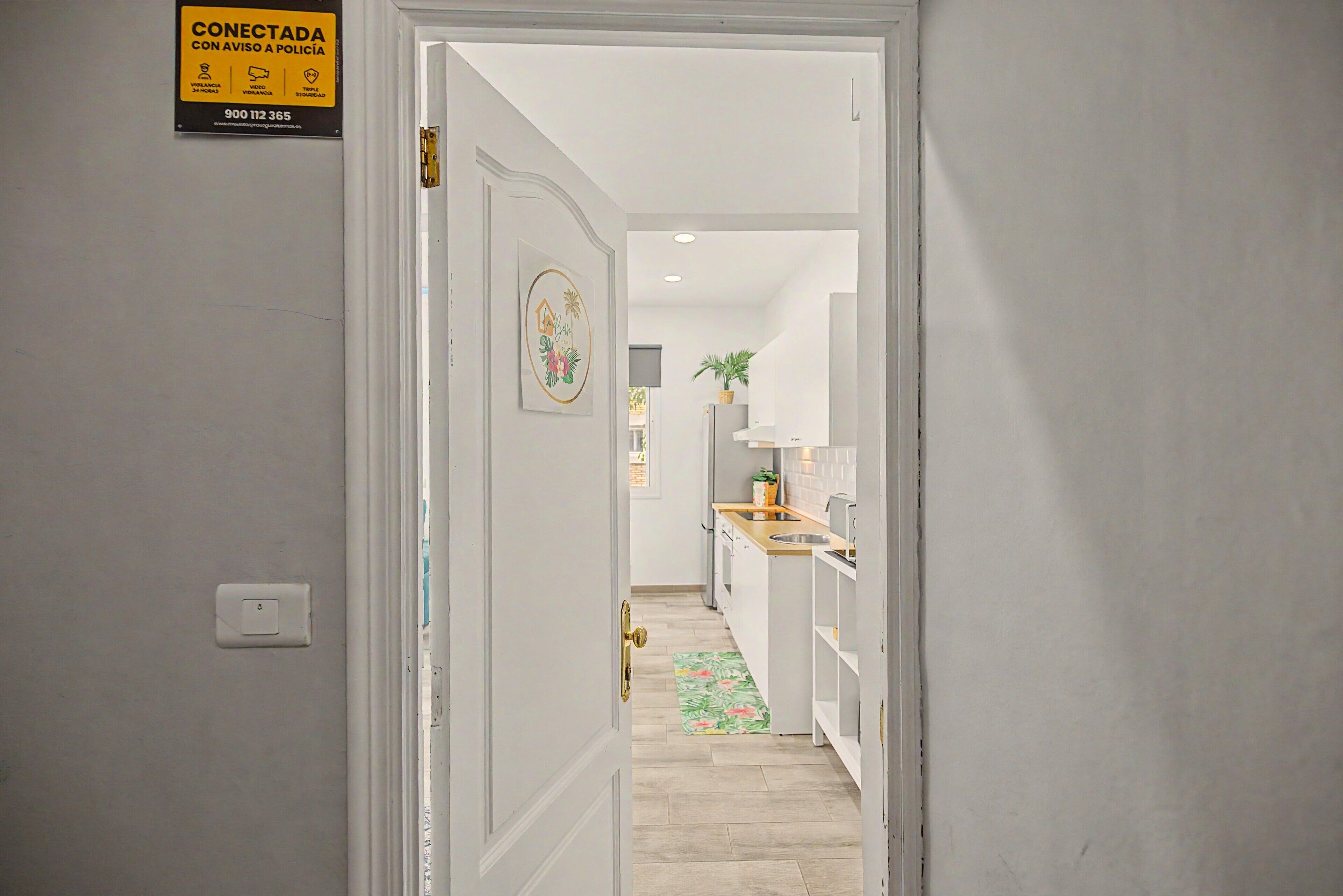 A hallway leading to a kitchen with a sign on the wall, a light switch, and a door.