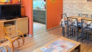 Una sala de estar moderna con televisor, muebles de madera y un comedor con manteles estampados.