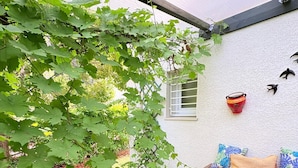 Un patio techado con un banco de madera, una mesita y una jardinera fijada a la pared.
