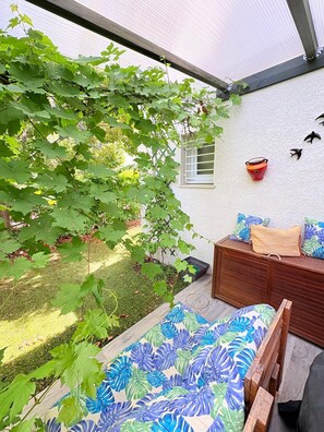 Eine überdachte Terrasse mit einer hölzernen Bank, einem kleinen Tisch und einem an der Wand befestigten Blumentopf.