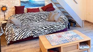 Una habitación tipo loft con techo inclinado, un sofá estampado con diseño de cebra, una mesa de centro de madera y una escalera.