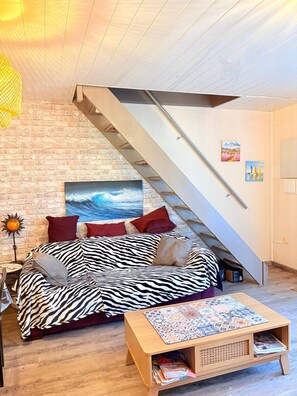 Ein Loft-Zimmer mit schrägem Dach, einem Sofa in ZEBRA-Muster, einem Holztisch und einer Treppe.