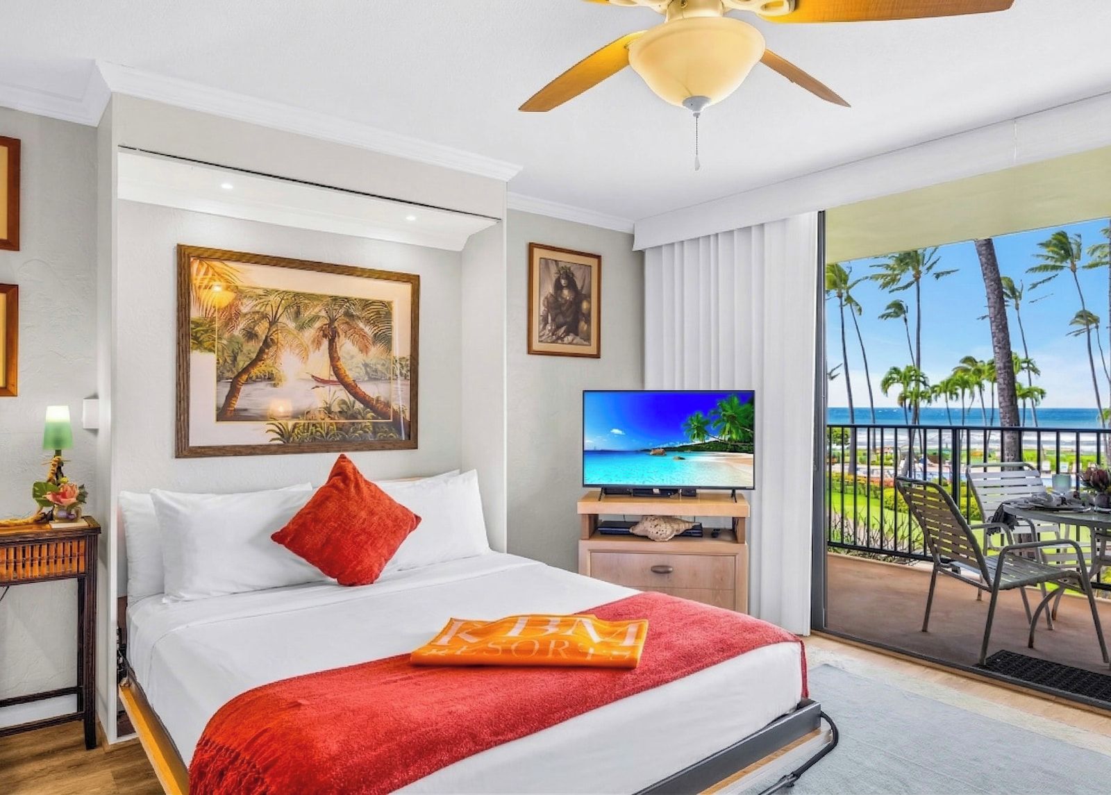 Une chambre d’hôtel équipée d’un lit, d’une télévision, d’un balcon avec vue sur l’océan et d’un ventilateur de plafond.