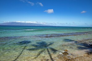 A clear view of a beach with shallow waters, rocks, and a distant mountain range. - Papakea Resort 2 Beachfront Villas, Sleeps 8 | Car Incl. w/ 6 nights | ML-4115 by KBM (Lahaina)