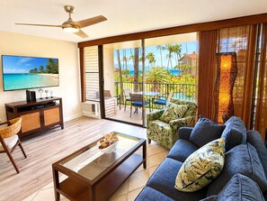 Ein Wohnzimmer mit einer Couch, einem Couchtisch, einem Fernseher und einem Balkon mit Meerblick.