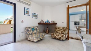 Un salon avec deux fauteuils à motifs, une cheminée et une vue sur la cuisine.