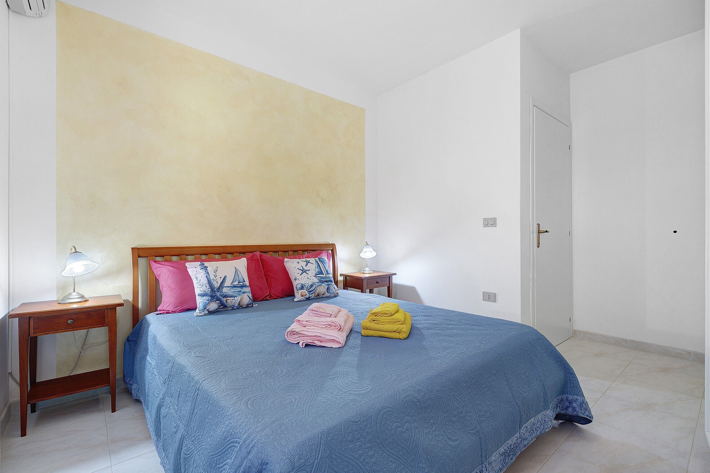A bedroom with a bed, two bedside tables, a nightstand, and a door.