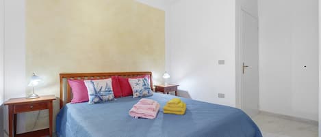 A bedroom with a bed, two bedside tables, a nightstand, and a door.