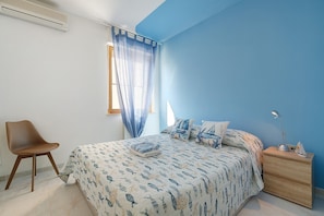 Una camera da letto con un letto, una sedia, un comodino e una finestra con tende.