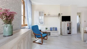 Un salon avec un fauteuil bleu, un téléviseur et un meuble.
