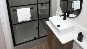 Un baño moderno con ducha envuelta en vidrio, un lavamanos blanco, un espejo grande y armarios de madera.