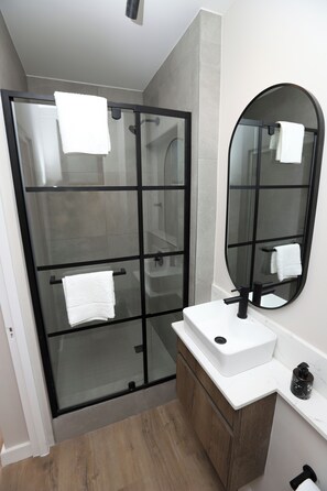 A modern bathroom with a glass-enclosed shower, a white sink, a large mirror, and wooden cabinets.