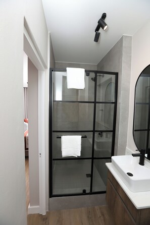 A modern bathroom with a glass-enclosed shower, a white sink, and a large mirror. - WINK Aparthotel Saxon Square (Johannesburg)