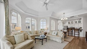 Un salon spacieux doté d’une grande fenêtre, d’un ventilateur de plafond et d’un coin repas agrémenté d’un lustre.