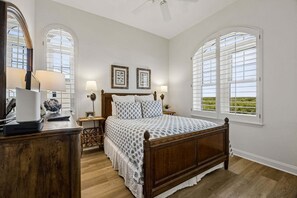 Ein Schlafzimmer mit einem Holzbett, zwei Nachttischen mit Lampen, einer Kommode und großen Fenstern mit Fensterläden.