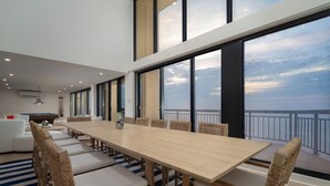 A spacious dining area with a long wooden table and wicker chairs, large windows offering a view of the sky and a balcony. - Newly renovated luxury retreat with incredible views, features 6 bedrooms and 5 baths! (Ocean City)