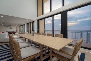 A spacious dining area with a long wooden table and wicker chairs, large windows offering a view of the sky and a balcony. - Newly renovated luxury retreat with incredible views, features 6 bedrooms and 5 baths! (Ocean City)