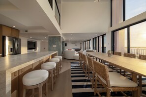 A modern kitchen with a long dining table, bar stools, and a large window. - Newly renovated luxury retreat with incredible views, features 6 bedrooms and 5 baths! (Ocean City)