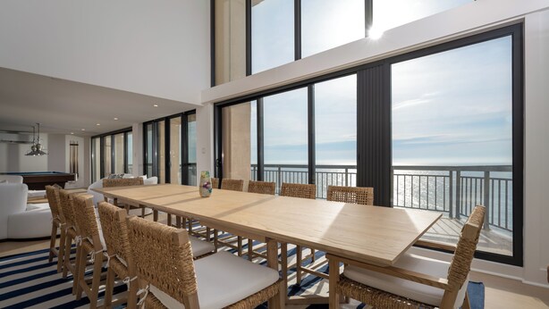 A modern dining area with a large table and wicker chairs, large windows with a view of the sea, and a striped floor. - Newly renovated luxury retreat with incredible views, features 6 bedrooms and 5 baths! (Ocean City)