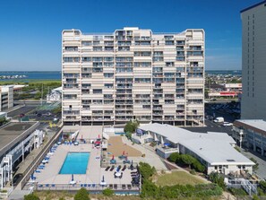 A multi-story hotel with a pool area, including sun loungers and umbrellas. - Newly renovated luxury retreat with incredible views, features 6 bedrooms and 5 baths! (Ocean City)