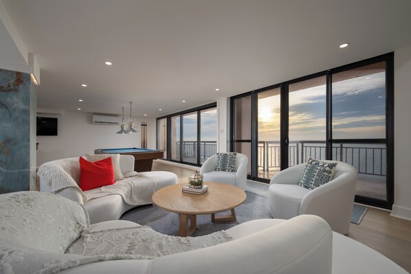 A modern living room with a pool table, large windows, and a view of the sky. - Newly renovated luxury retreat with incredible views, features 6 bedrooms and 5 baths! (Ocean City)