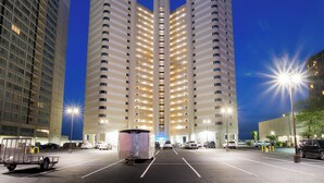 Un edificio de gran altura con varios pisos, un estacionamiento al frente y una caravana en primer plano.
