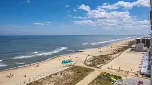 Ein Strand mit blauem Himmel, sandigem Ufer und einigen Gebäuden im Hintergrund.