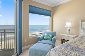 A bedroom with a view of the ocean, a chair with a pillow, a bedside table with a lamp, and a bed with a patterned bedspread. - Three bedroom oceanfront condo in the luxurious Gateway Grand! (Ocean City)