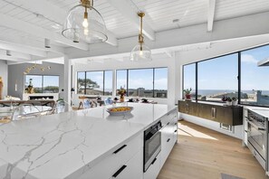 A modern kitchen with a large island, built-in appliances, and large windows offering a view of the city. - Artist Haven This custom contemporary home showcases the best of Bodega Bay! (Bodega Bay)