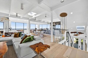 A spacious living area with a white sofa, a wooden coffee table, and a dining area with a glass railing. - Artist Haven This custom contemporary home showcases the best of Bodega Bay! (Bodega Bay)