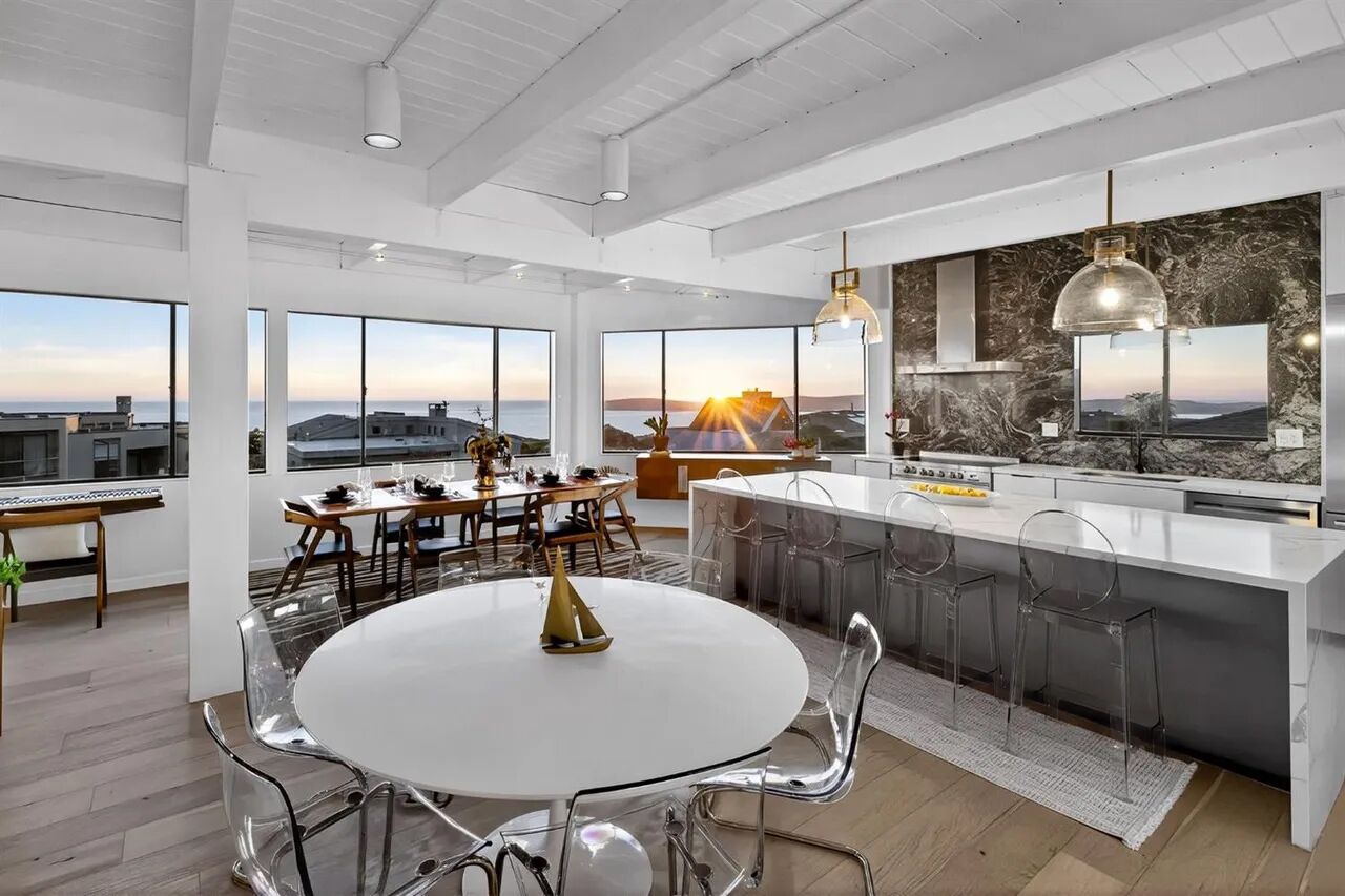 Cozinha moderna com uma ilha grande, área de jantar com mesa redonda e grandes janelas com vista para o pôr do sol.