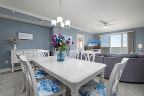 A dining area with a white table and chairs, a vase with flowers, and a gray sofa in the background. - Gateway Grand 510 Storage locker included and new decorator furnishings!! (Ocean City)