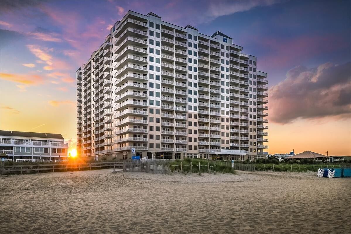 Ein Hochhaus-Hotel mit mehreren Balkonen, gelegen nahe am Strand, mit Sonnenuntergang im Hintergrund.