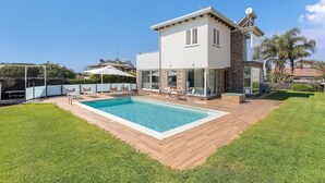 Ein modernes Haus mit Swimmingpool, Terrassenmöbeln und blauem Himmel.