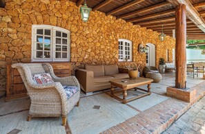 A stone-walled outdoor seating area with a sofa, a wicker chair, and a wooden table. - Villa Goffrey, Sicily (San Ciro - Ulmi - Filci)