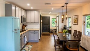 A kitchen with white cabinets, a blue refrigerator, and a dining area with a table and chairs. - Rustic Retreat with Private Pond, Gazebo & Creek in Andes, New York (Andes)