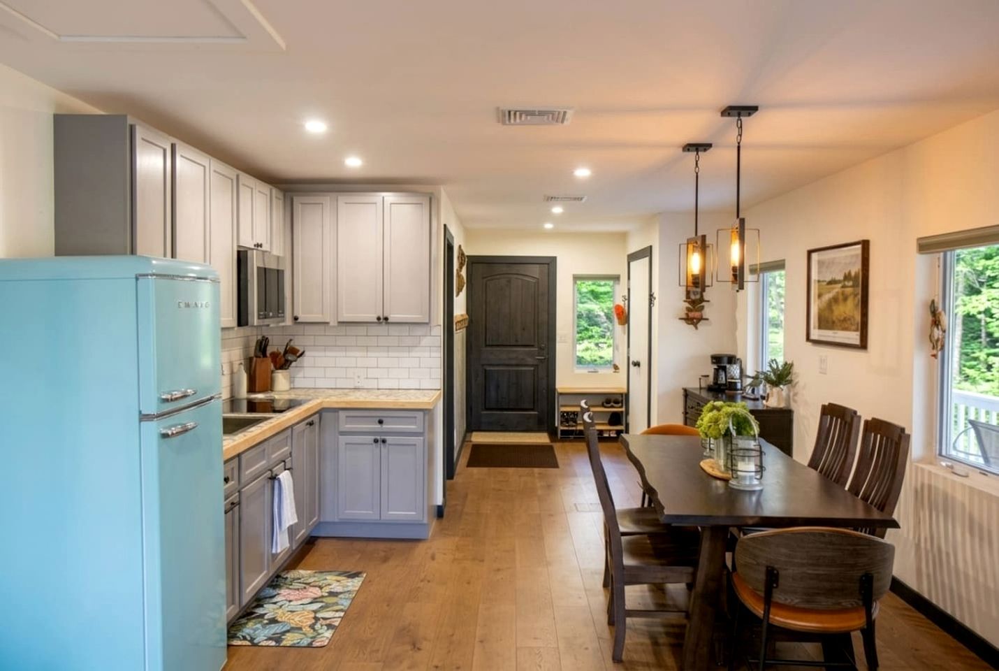Una cocina con armarios blancos, un refrigerador azul y un comedor con mesa y sillas.