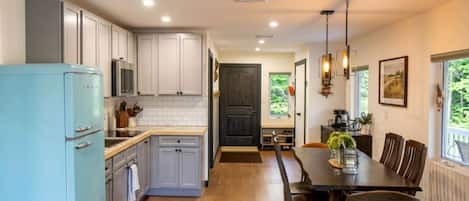 Una cocina con armarios blancos, un refrigerador azul y un comedor con mesa y sillas.