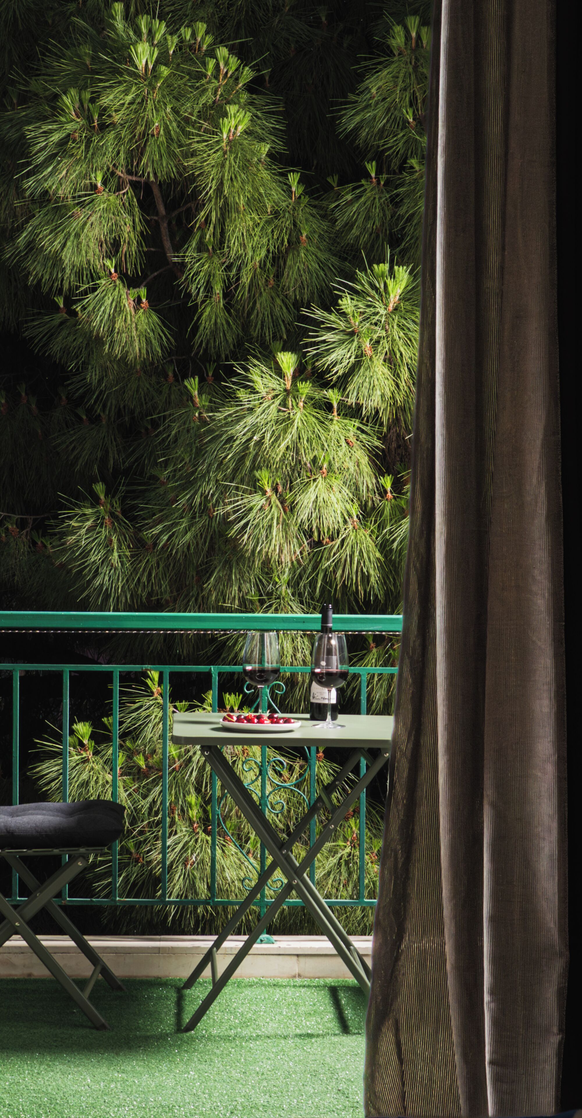 Een balkon met een eettafel, een stoel en uitzicht op een dichte dennenboom.