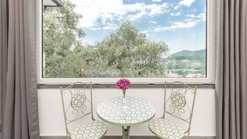 Un balcone con tavolo e due sedie, un vaso con un fiore e vista su alberi e colline.